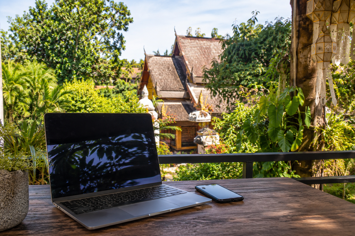 Illustration of a laptop and smartphone overlooking a leafy Chiang Mai garden.